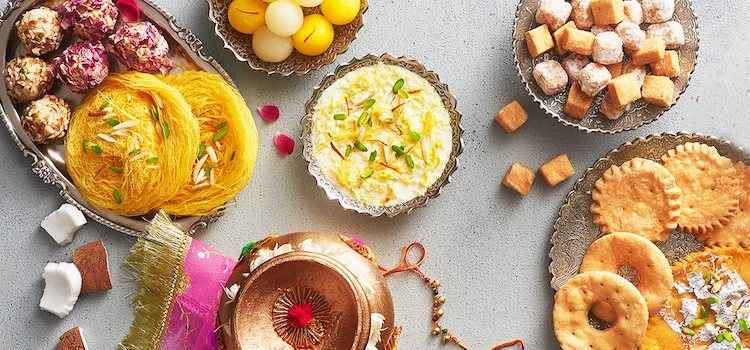 Assorted traditional Indian sweets in decorative silver bowls — rasmalai, laddus, barfi and more